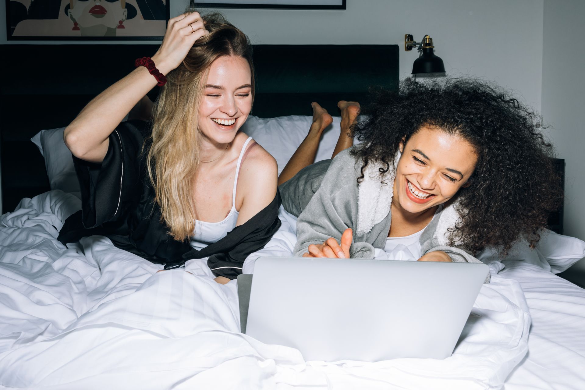 Two friends laughing together while taking a fun online personality quiz on a laptop, one pointing at the screen in delight